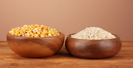 Raw corn and wheat in wooden bowls on table on brown background