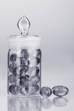 Transparent bottle with pills in grey light isolated on white