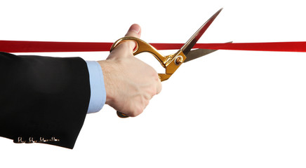 Man's hand cutting red ribbon with pair of scissors isolated