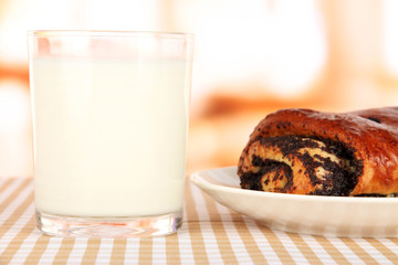 Poppy roll and glass of milk on room background