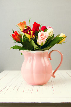 Rose flowers in pink jug on wooden table