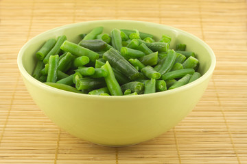 Green beans in a bowl on a wicker mat close up