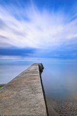 Concrete pier or jetty on a blue sea and cloudy sky. Normandy