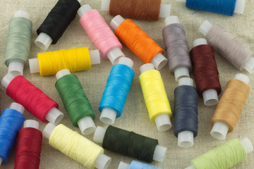 Lot of colored thread spools on beige fabric close up