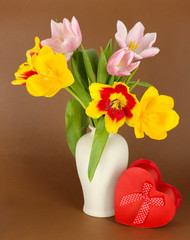 Beautiful tulips in bucket with gift on brown background