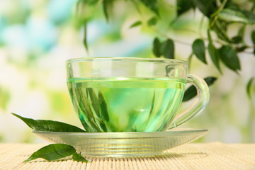 Transparent cup of green tea on bamboo mat, on nature