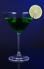 Green cocktail in martini glass on dark blue background