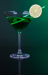 Green cocktail in martini glass on dark green background