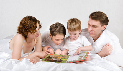 Obraz na płótnie Canvas Parents with children are reading book in the bed