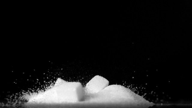 Sugar Cubes Falling Into Pile Of Sugar On Black Background