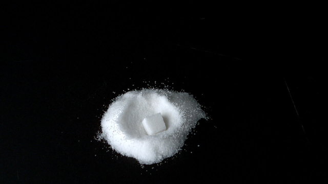 Sugar cube falling into pile of sugar on black surface