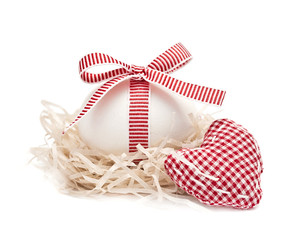 White egg in a nest with red ribbon and bow, heart