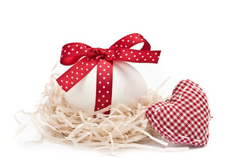 White egg in a nest with red ribbon and bow, heart