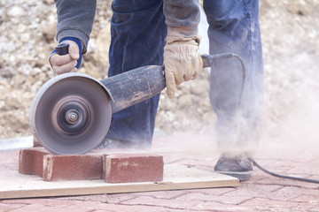 worker uses a stone cutter to cut the brick pavers