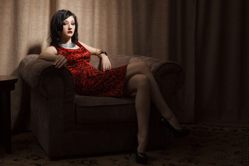 Attractive young woman in red dress sitting on chair in hotel