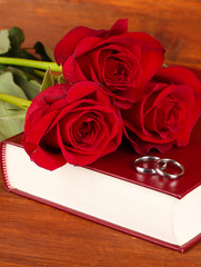 Wedding rings on bible with roses on wooden background