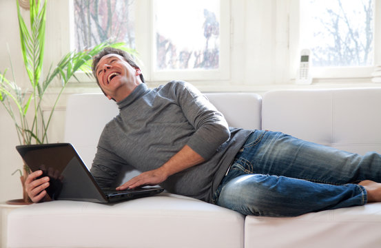 Mann mit Laptop Zuhause auf dem Sofa liegend