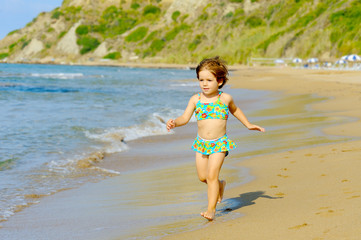 Happy toddler girl running on the beach