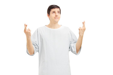 Male patient in a hospital gown with fingers crossed posing