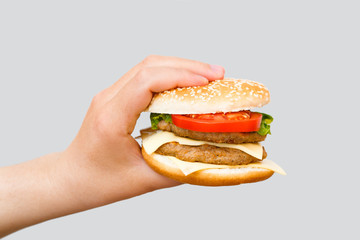 Hand holding delicious fast food cheeseburger on grey background