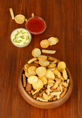 Crackers in wooden bowl and sauces, on wooden background