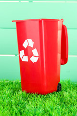 Recycling bin on grass on light blue background