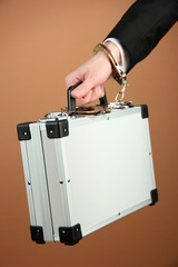 Hand with handcuff and suitcase, on color background