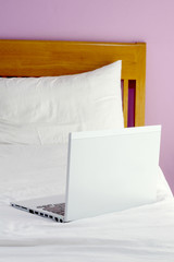 white laptop on white bed in the morning