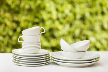 Clean dishes and cups on white tablecloth on green background