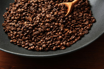 Black wok pan with coffee beans on wooden table, close up