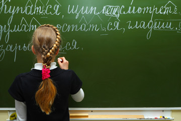The schoolgirl writes chalk on a blackboard