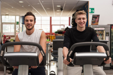 Young smiling men training in the gym with bike.