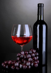 Red wine glass and bottle of wine on grey background