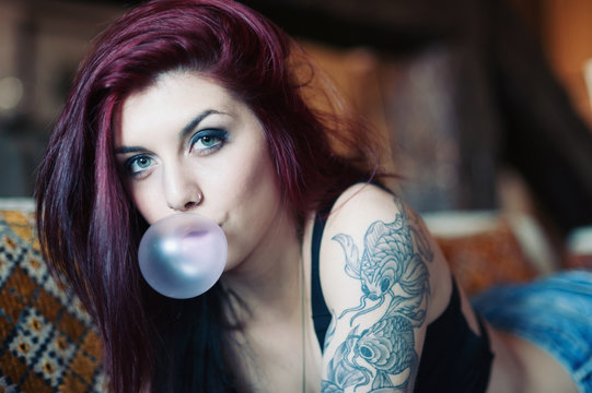Sensual portrait of tattooed red head girl with chewing gum.