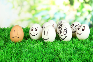 Eggs with funny faces on grass on bright background