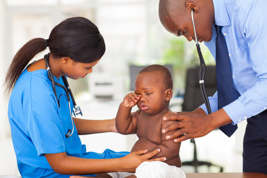 Afro American Pediatrician And Nurse Examining A Baby Boy