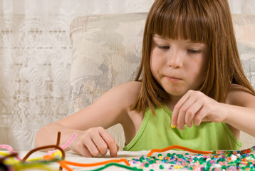 Obraz na płótnie Canvas Young girl making a bead bracelet