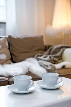 Two coffee cups on the table with sofa with fur cover on it