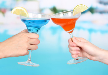 Cocktails in men's and women's hands on pool background