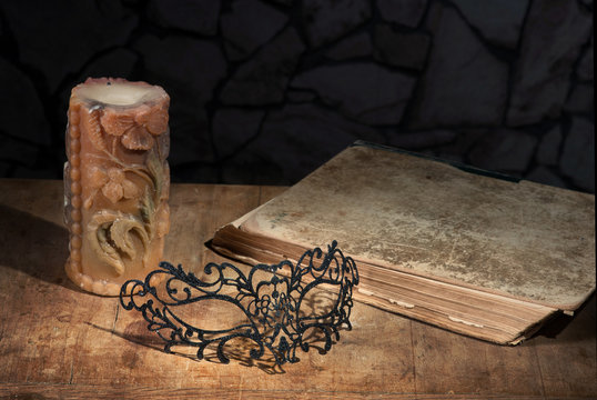 Vintage still life with lacy mask, ancient book and candle