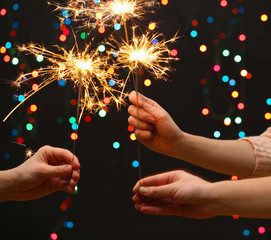 beautiful sparklers in woman hands on garland background.