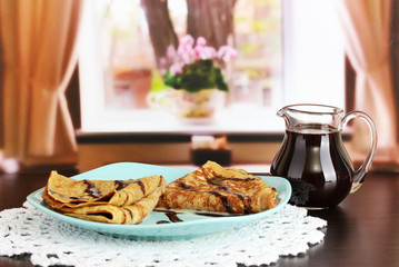 Sweet pancakes on plate with condensed milk on table in room