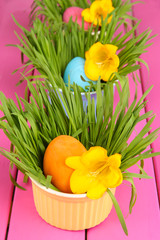 Easter eggs in bowls with grass on pink wooden table close up