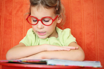 Girl with glasses reading a book intently.