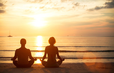 Young couple doing yoga on the beach