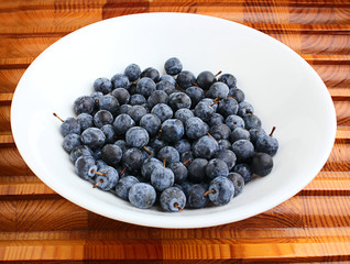 Ripe blackthorn in the plate on a wooden background