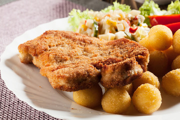 Breaded chop, prepared potatoes and salad. Mysterious light.