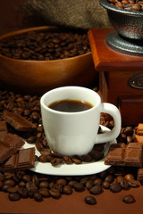 cup of coffee, grinder and coffee beans on brown background