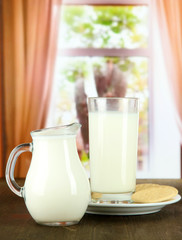 Glass of milk, a jug and cookies on a room background