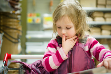 Adorable girl in shopping cart select books on shelves in superm